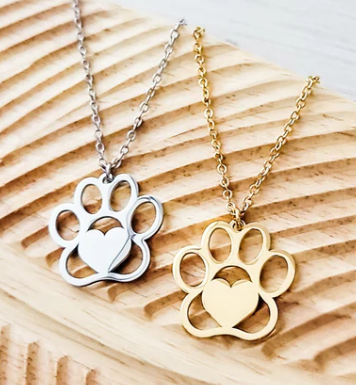 Two paw-shaped necklaces, one silver and one gold, on a wooden surface.