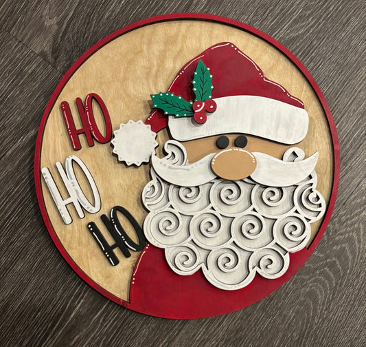 A 12" circular decorative sign featuring a stylized Santa Claus with 'HO HO HO' text around, predominantly in red and white colors.
